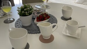A dining table set with white cups, a pitcher, and a bowl of strawberries. A potted plant is on the table, and a bed with white bedding is in the background. - Luxuroese Apartments mit Privatem Pool und Jacuzzi (Biograd na Moru)