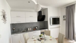 A modern kitchen with white cabinets, a grey countertop, and a built-in oven. There is a dining table with chairs and a chandelier above. - Luxuroese Apartments mit Privatem Pool und Jacuzzi (Biograd na Moru)