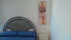 A small bedroom with a bed, a nightstand, a lamp, and a wall-mounted artwork.