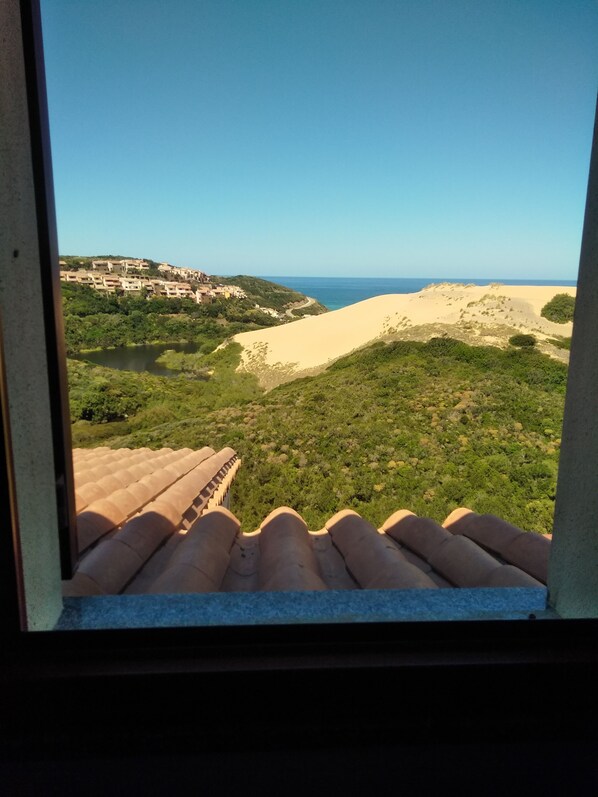 Vista desde una ventana que da a un paisaje costero con dunas de arena y un pueblo lejano.