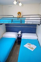 Habitación con literas, dos camas, una mesita de noche con lámpara y un oso de peluche en la litera superior.