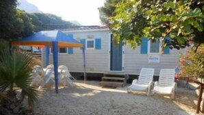 A mobile home with a covered patio area, two lounge chairs, and a small play structure. - Happy Camp in El Bahira Camping Village (San Vito Lo Capo)