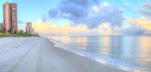 A beach with a clear path leading to the water, tall buildings in the background, and a partly cloudy sky. - BEST LOCATION in Naples Park! Beach, Bikes, & Firepit (Naples)