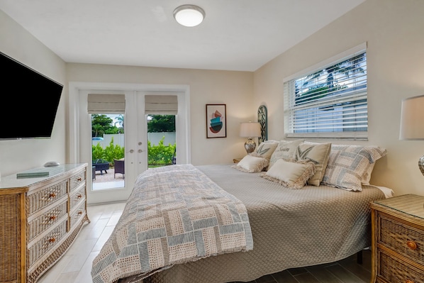A bedroom with a bed, a TV, a desk, and a window with blinds.