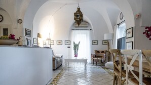 Een ruime woonkamer met een hoge gewelfde plafond, een centrale salontafel en een eethoek met stoelen.