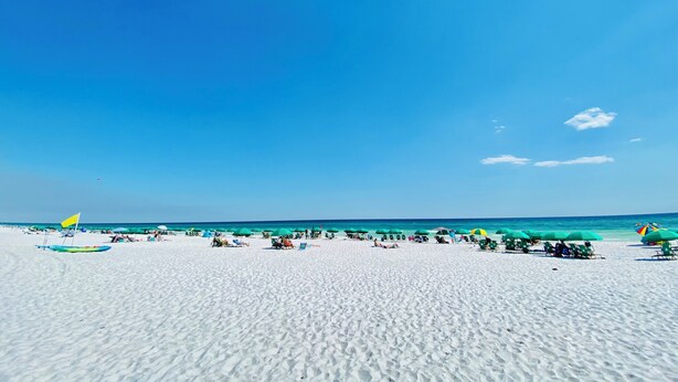 Une plage de sable blanc, un ciel bleu azur et l’océan.
