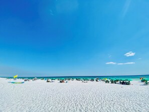 A beach with white sand, clear blue sky, and ocean.