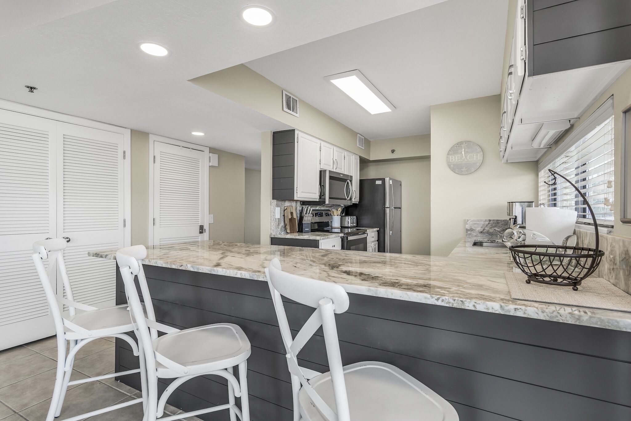 A kitchen with a marble countertop, white chairs, and modern appliances.
