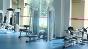 A gym with various exercise equipment, large windows, and a blue floor. - Grand Nest Hotel (Zhuhai)