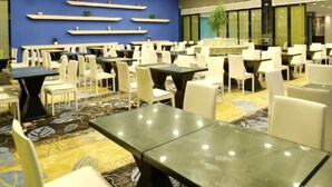 A restaurant with multiple tables and chairs, a blue wall with shelves, and hanging pendant lights. - Grand Nest Hotel (Zhuhai)