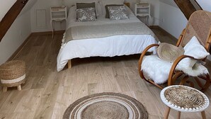 Une chambre mansardée chaleureuse, avec un plafond en pente, un lit agrémenté d'oreillers à motifs, un fauteuil en osier et une petite table d'appoint.