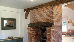 Une pièce avec une cheminée en briques, des poutres apparentes, un meuble vert et un sol carrelé.