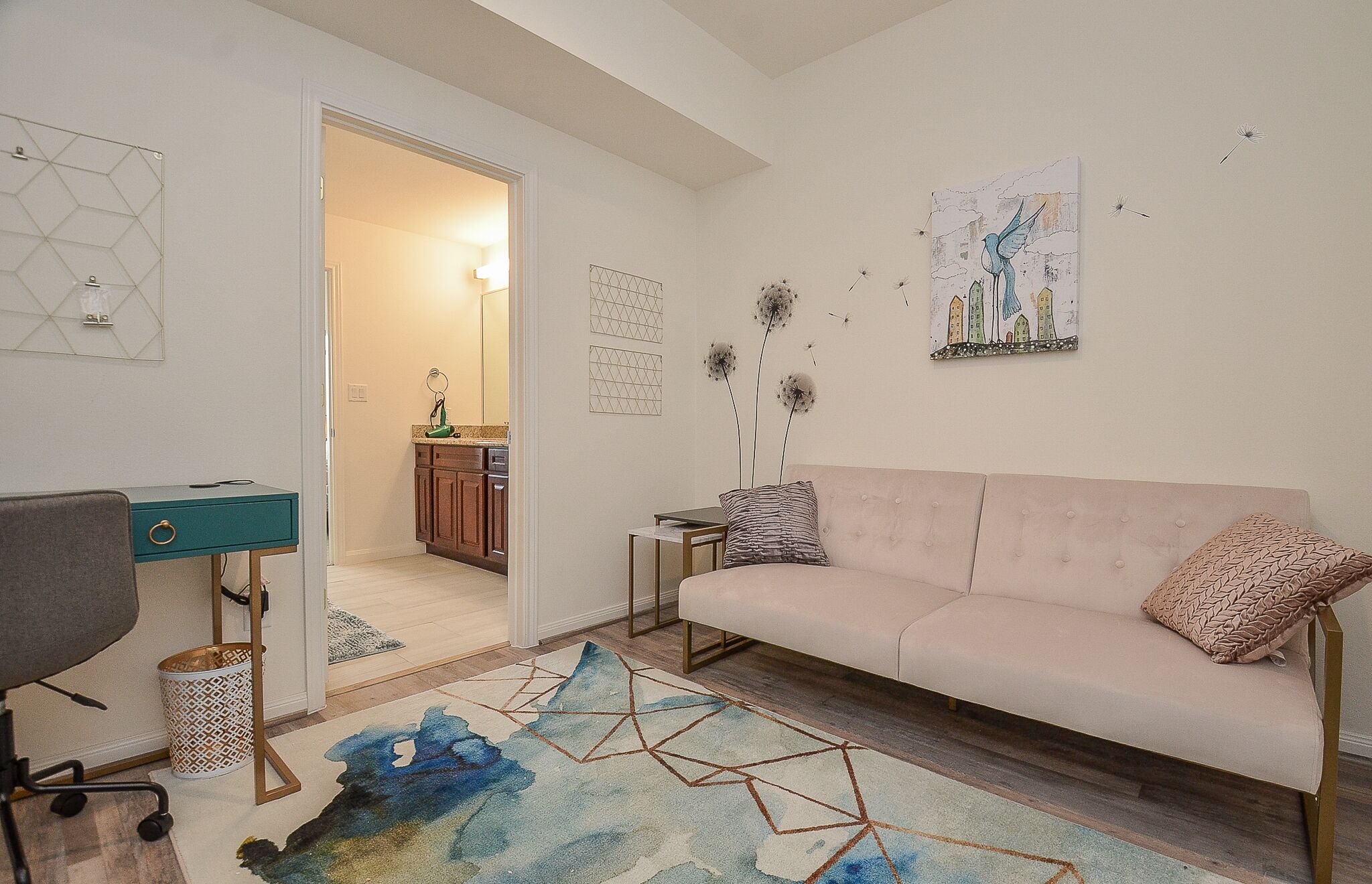 Un salon avec un canapé, un bureau et une chaise. Une porte donne accès à une autre pièce.