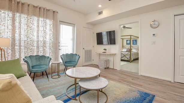 Un salon moderne comprenant un canapé, deux fauteuils, une table basse ronde et un téléviseur fixé au mur.