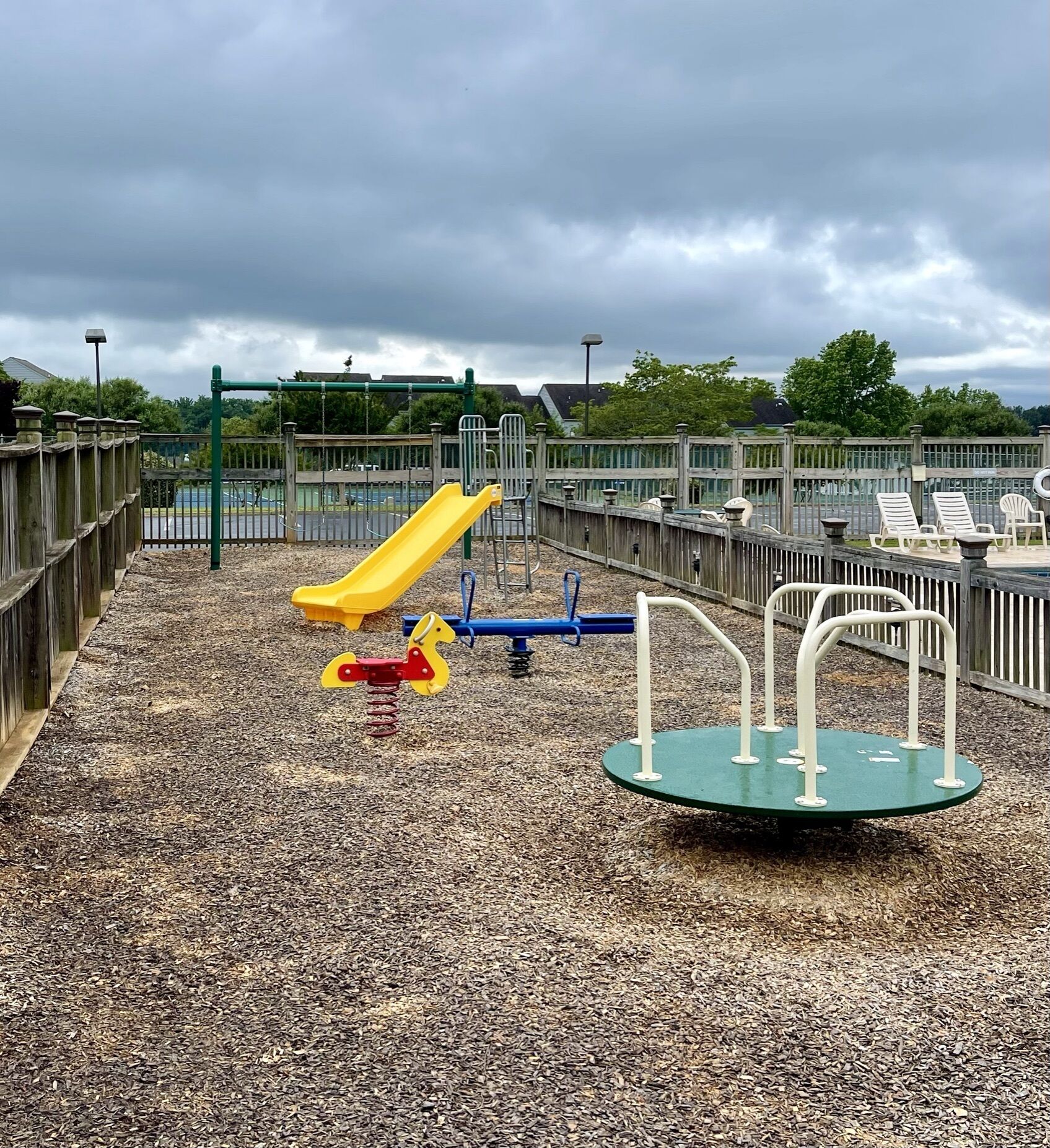 Un parque infantil con un tobogán amarillo, columpios y un carrusel.