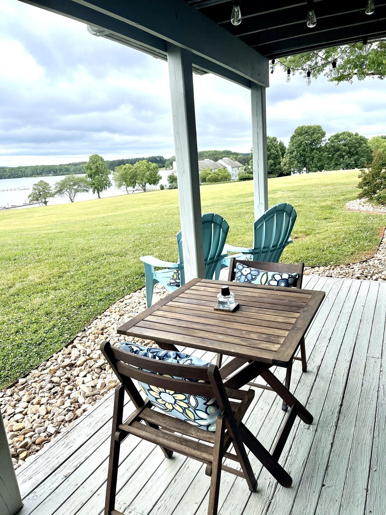A wooden deck with a table and chairs, overlooking a grassy area and a body of water.