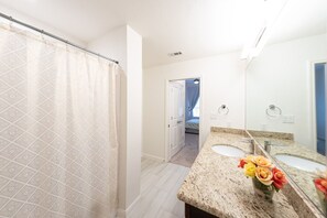A bathroom with a shower curtain, a sink with a vase of flowers, and a mirror. - Spacious Private Condo Unit in Lifestyle Center (Katy)