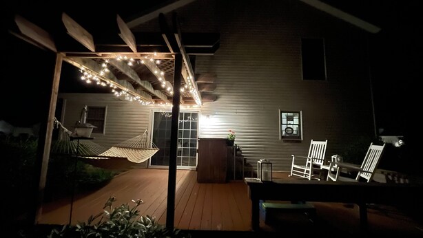 Een terras buiten met lichtslingers, een hangmat en tuinmeubels.