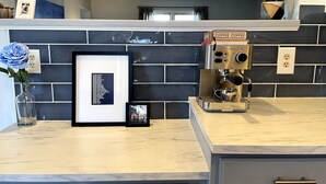 Een keuken met een koffieapparaat, ingelijste foto's en een vaas met een blauwe bloem.
