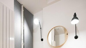 Una habitación con un sofá amarillo, dos mesas redondas negras, un espejo circular y dos lámparas de pared.