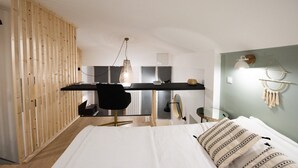 Un dormitorio con cama, escritorio y silla. Se observa un armario de madera a la izquierda y una decoración de macramé en la pared derecha.