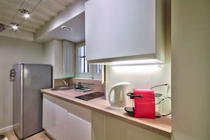 Eine kleine Küche mit einem Kühlschrank, einem Wasserkocher und einer roten Kaffeemaschine auf der Arbeitsfläche.
