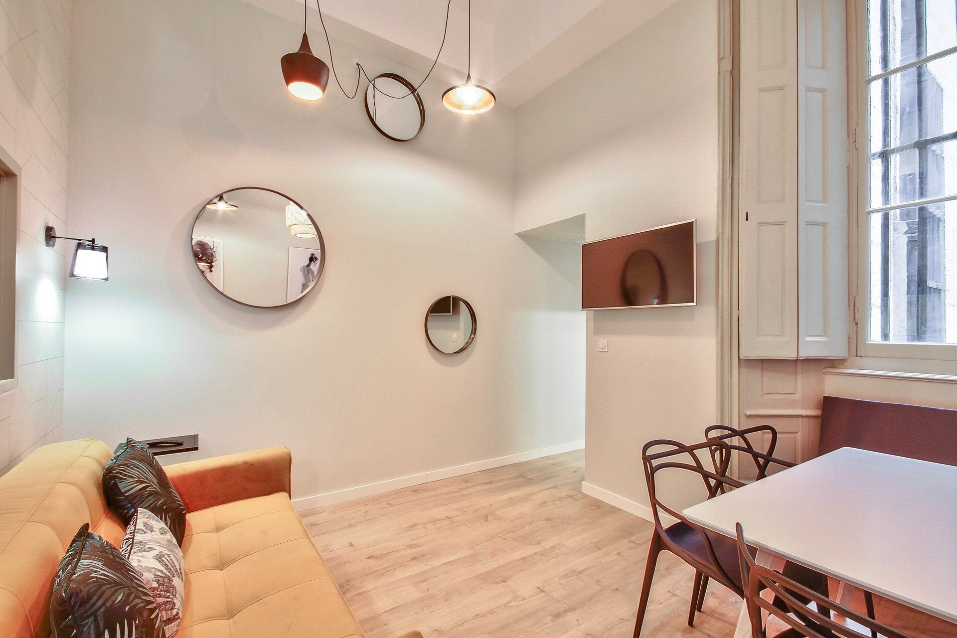 Un salon moderne avec un canapé, une table à manger et des chaises. On y trouve trois miroirs fixés au mur et des luminaires suspendus.