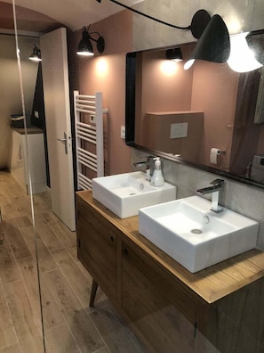 A modern bathroom with two white sinks, a wooden vanity, a towel rack, and a large mirror.