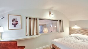 A bedroom with a bed, a desk with a lamp, a framed abstract artwork, a window with curtains, and a wall-mounted light fixture. - Quiet and cozy 3-bedroom flat – Terreaux/Opéra (Lyon)