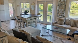 Un vaste espace de vie comprenant un salon avec une table basse en verre, un canapé agrémenté de coussins à motifs et un coin repas avec une table et des chaises en bois.