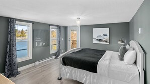 Une chambre à coucher avec un lit, une fenêtre avec des rideaux, un tableau accroché au mur et un luminaire au plafond.