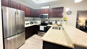 A modern kitchen with stainless steel appliances, dark wood cabinets, a granite countertop, and a skylight. - 1K| Spacious Home in Gated Complex| Walk to your Daily Needs (Katy)