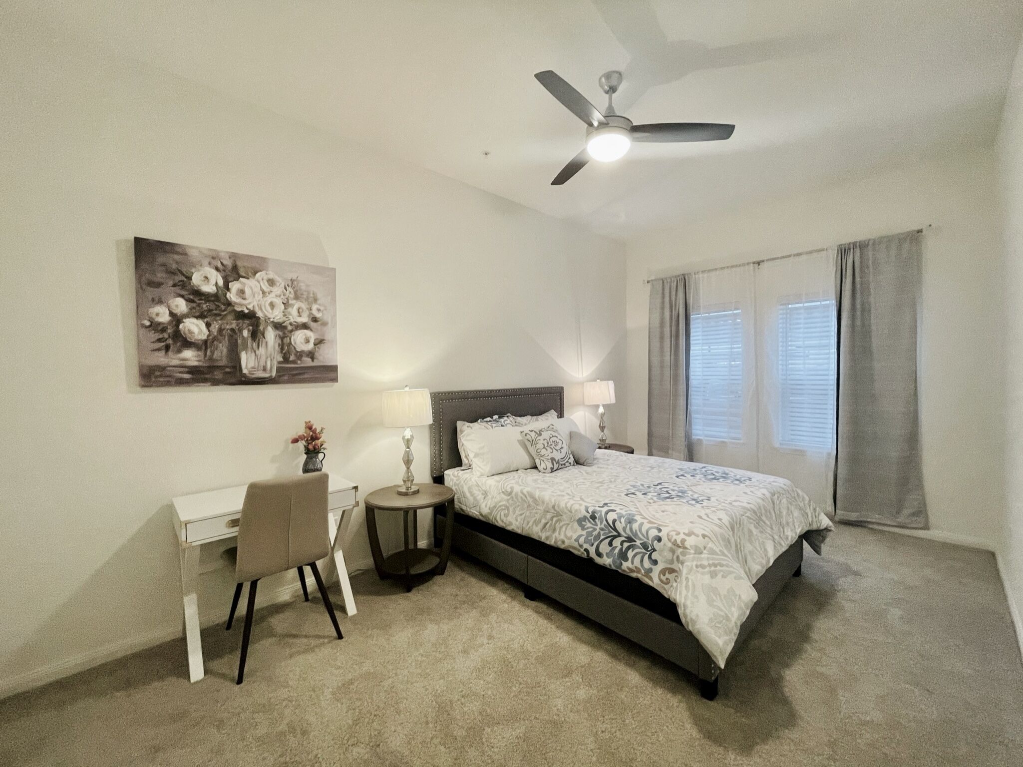 Une chambre à coucher comprenant un lit, un bureau, une chaise, une lampe et un ventilateur de plafond.