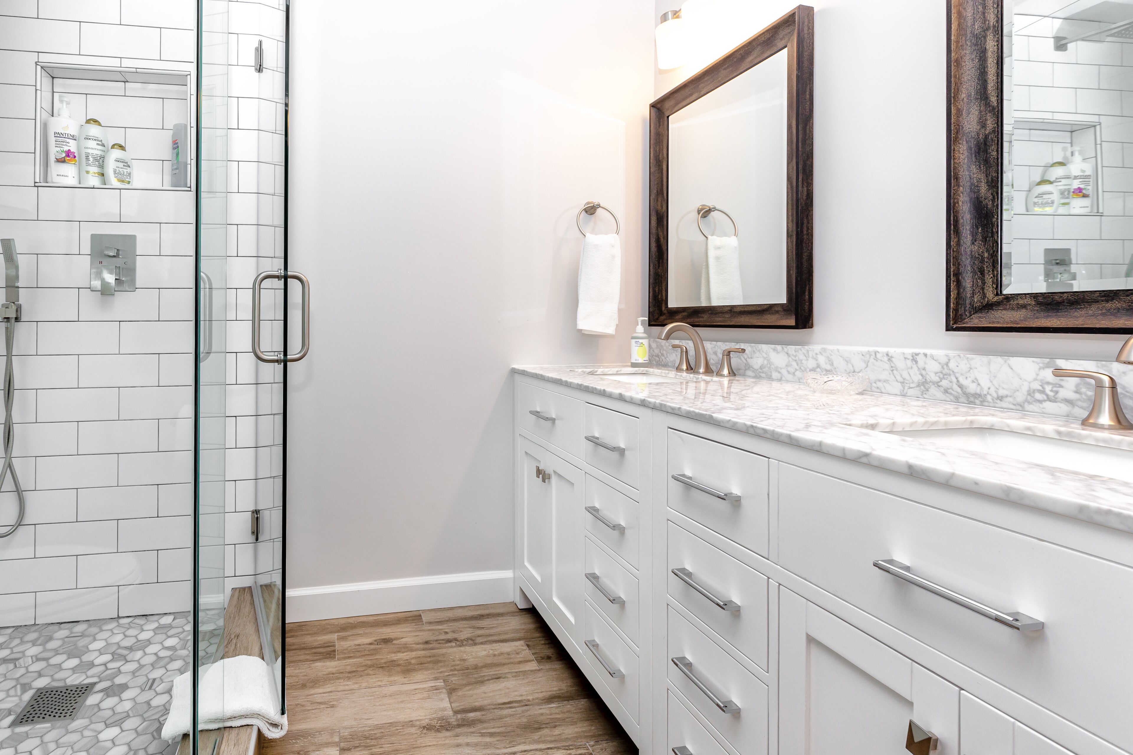 A modern bathroom with a glass shower enclosure, white tiled walls, and a marble countertop.