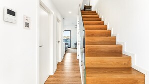 A modern staircase with wooden steps and glass railings, leading to a room with a bed and a view of the outdoors. - GuestReady - Freixo Island - Douro Views (Porto)