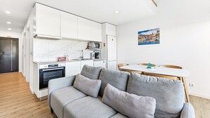 A compact living space with a kitchenette, a dining area, and a sofa with cushions. - GuestReady - Freixo Island - Douro Views (Porto)
