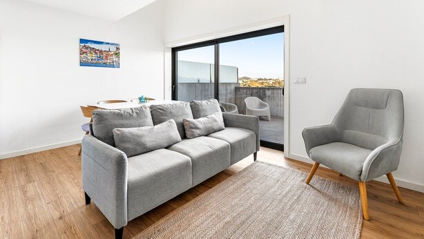 A modern living room with a grey sofa, a grey armchair, a wooden floor, and a large window. - GuestReady - Freixo Island - Douro Views (Porto)