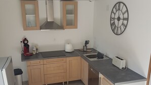 A modern kitchen with wooden cabinets, a stainless steel refrigerator, a built-in oven, a sink, and a clock on the wall.