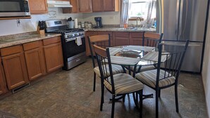 Una cocina con armarios de madera, un refrigerador de acero inoxidable, una estufa a gas y una mesa de comedor con sillas.