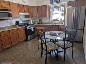 Una cocina con armarios de madera, un refrigerador de acero inoxidable, una estufa a gas y una mesa de comedor con sillas.