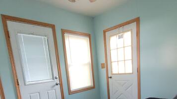 A room with a ceiling fan, a door with a window, a light-colored wall, a dark-colored couch, and a patterned rug.