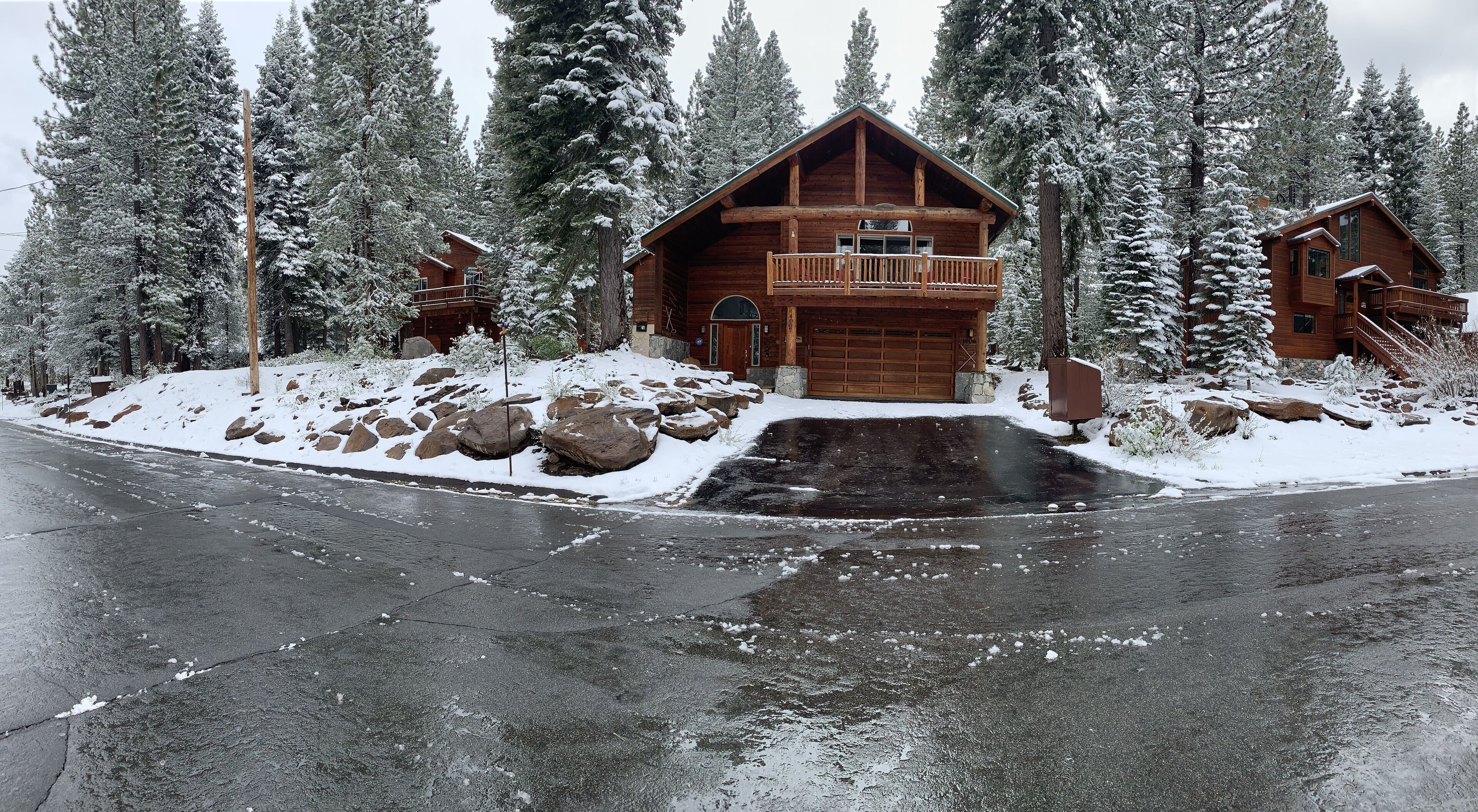A log cabin with a balcony, surrounded by snow-covered trees and rocks.