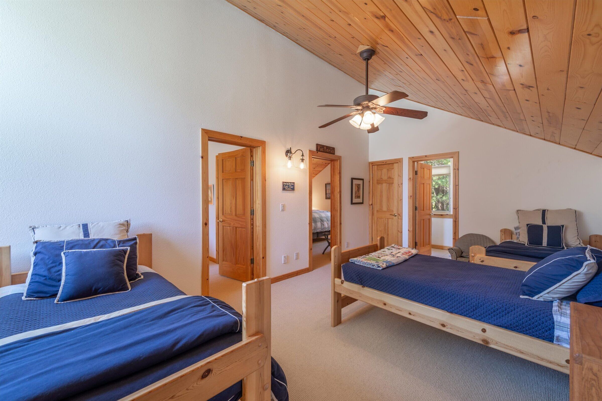 A room with two wooden beds, a ceiling fan, and wooden doors leading to other rooms.