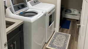 Ein kleiner Waschbereich mit einer Frontlader-Waschmaschine und -Trockner, einem Teppich und einer Futterstelle für Haustiere.