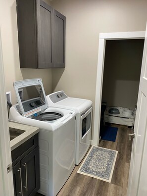 Uma área de lavanderia compacta com máquina de lavar e secar de abertura frontal, um tapete pequeno e um cantinho para alimentação de animais de estimação.