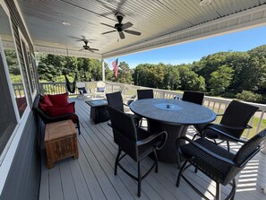 A covered outdoor deck with a round table and chairs, a small wooden cabinet, and a hammock. - Spacious Frankfort Getaway - Walk to Downtown and Lake Michigan - Sleeps 12-14. (Frankfort)