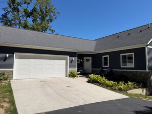 A residential house with a garage, a front porch with chairs, and a stone foundation. - Spacious Frankfort Getaway - Walk to Downtown and Lake Michigan - Sleeps 12-14. (Frankfort)
