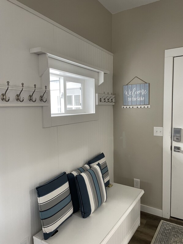Ein Zimmer mit einer weißen Bank, gestreifter Dekokissen, einem Fenster und einem Willkommensschild.