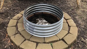 Ein Holzschaukelstuhl und eine Feuerstelle aus Metall mit Backsteingrund.