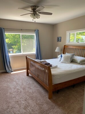 Quarto com cama de madeira, ventilador de teto, janela com cortinas e luminária.